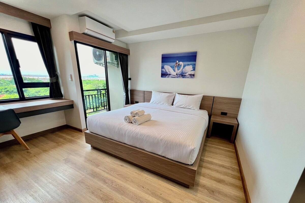 A modern hotel room with a large bed, a desk, and a balcony with a view.