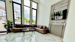 Et moderne venteområde med en hjørnesofa, et glasbord og et stort vindue med udsigt til gaden.