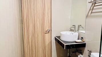 Un baño moderno con puerta de madera, lavamanos blanco, espejo y retrete.