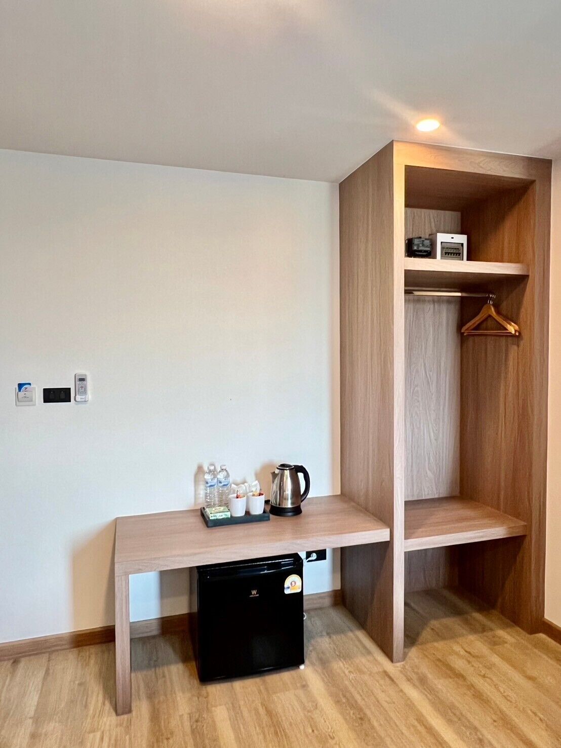 Una habitación compacta con escritorio de madera, refrigerador negro, armario de madera y perchero.