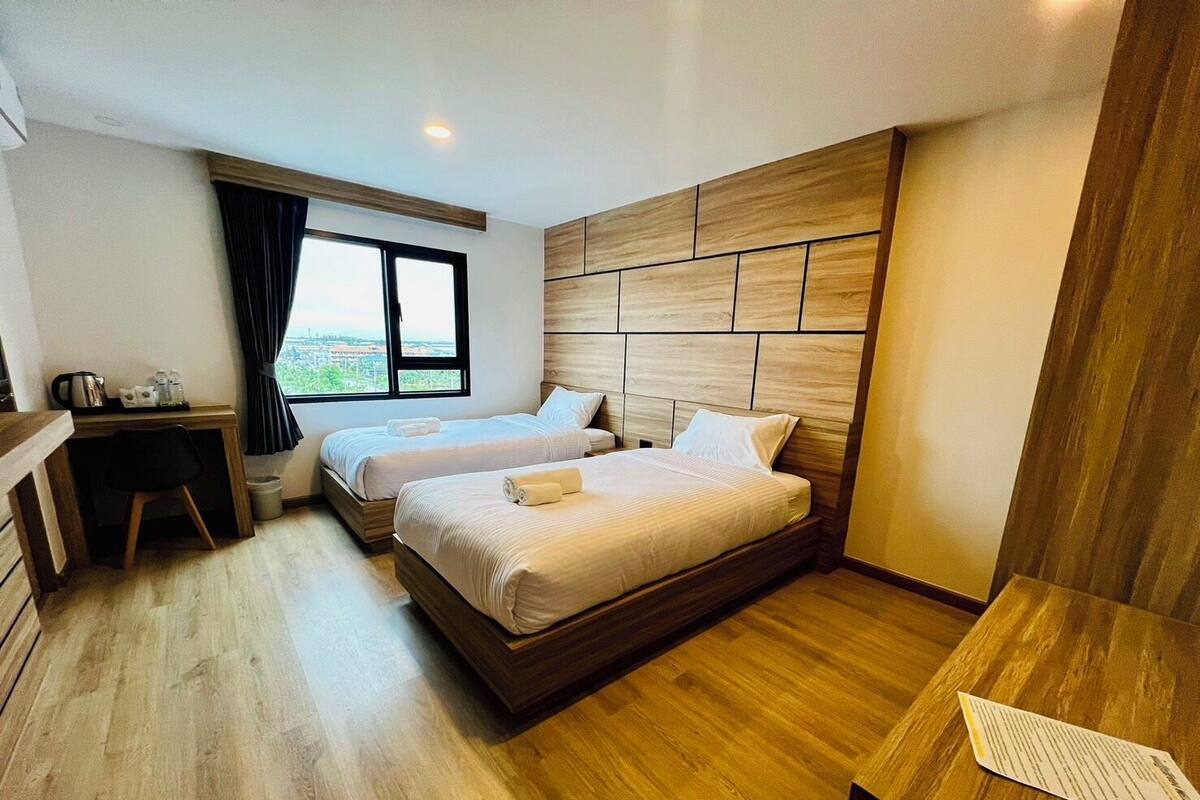A hotel room with two beds, a desk, and a view of the city.