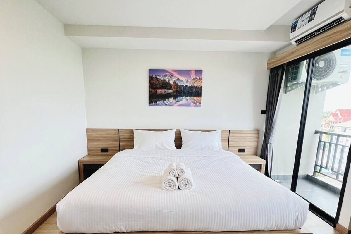 A modern bedroom with a large bed, wooden headboard, and a painting of a mountain landscape.