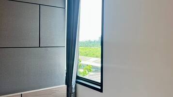 Un dormitorio moderno con cabecera integrada, una mesita de noche pequeña y una ventana con vistas a zonas verdes.