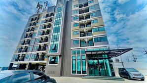 Et moderne hotel med flere etager, med altaner på hver etage, en overdækket indgang og en parkeringsplads med biler.