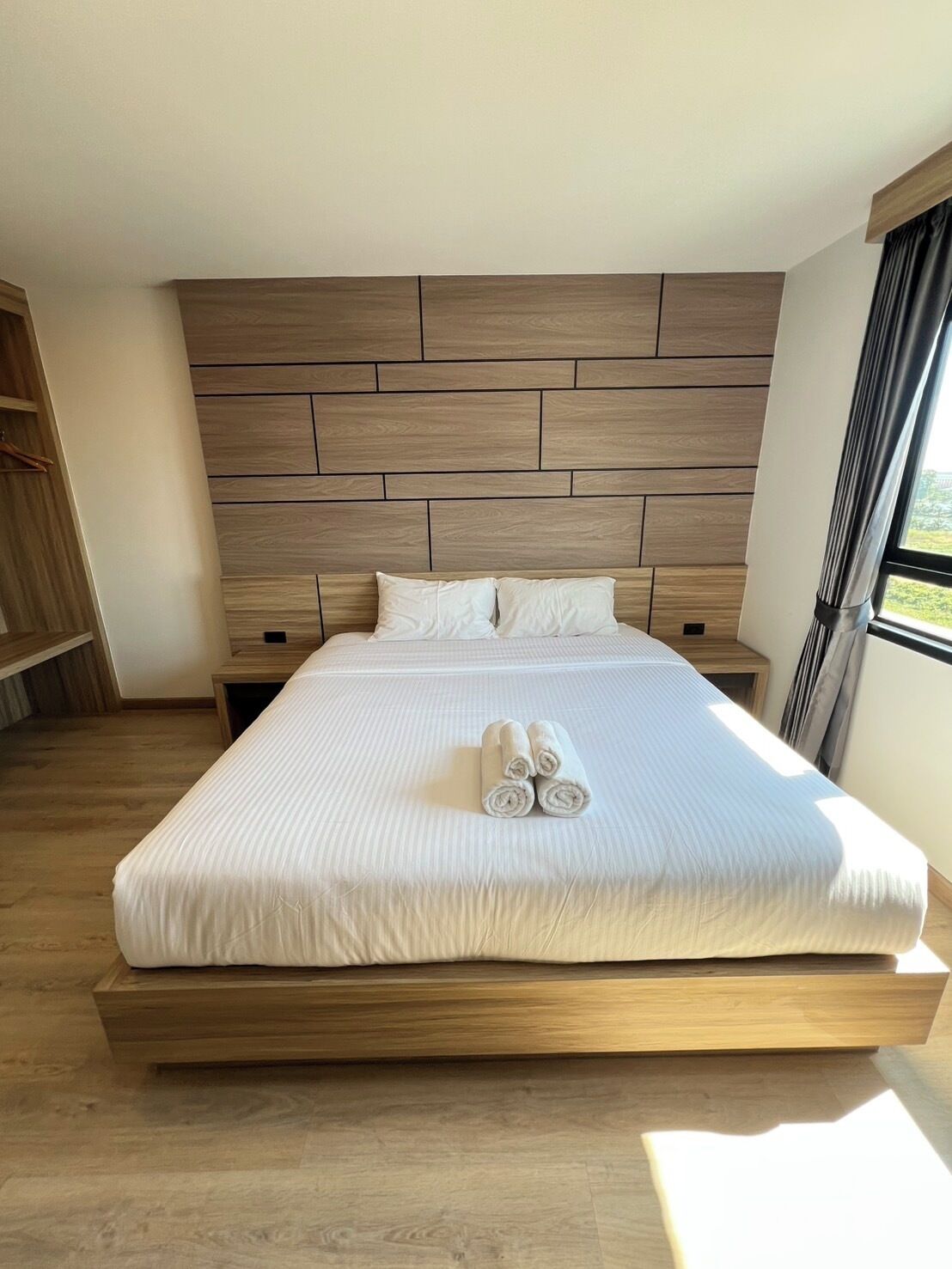 A modern hotel room with a large bed, wooden headboard, and a view of the outdoors.