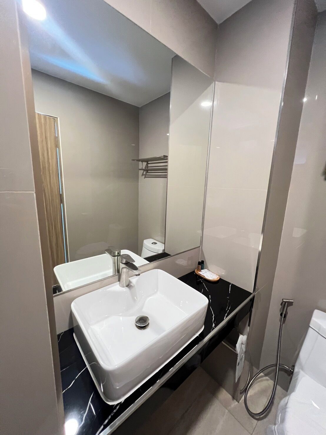 Un baño moderno con un lavamanos blanco, un espejo y una encimera negra.