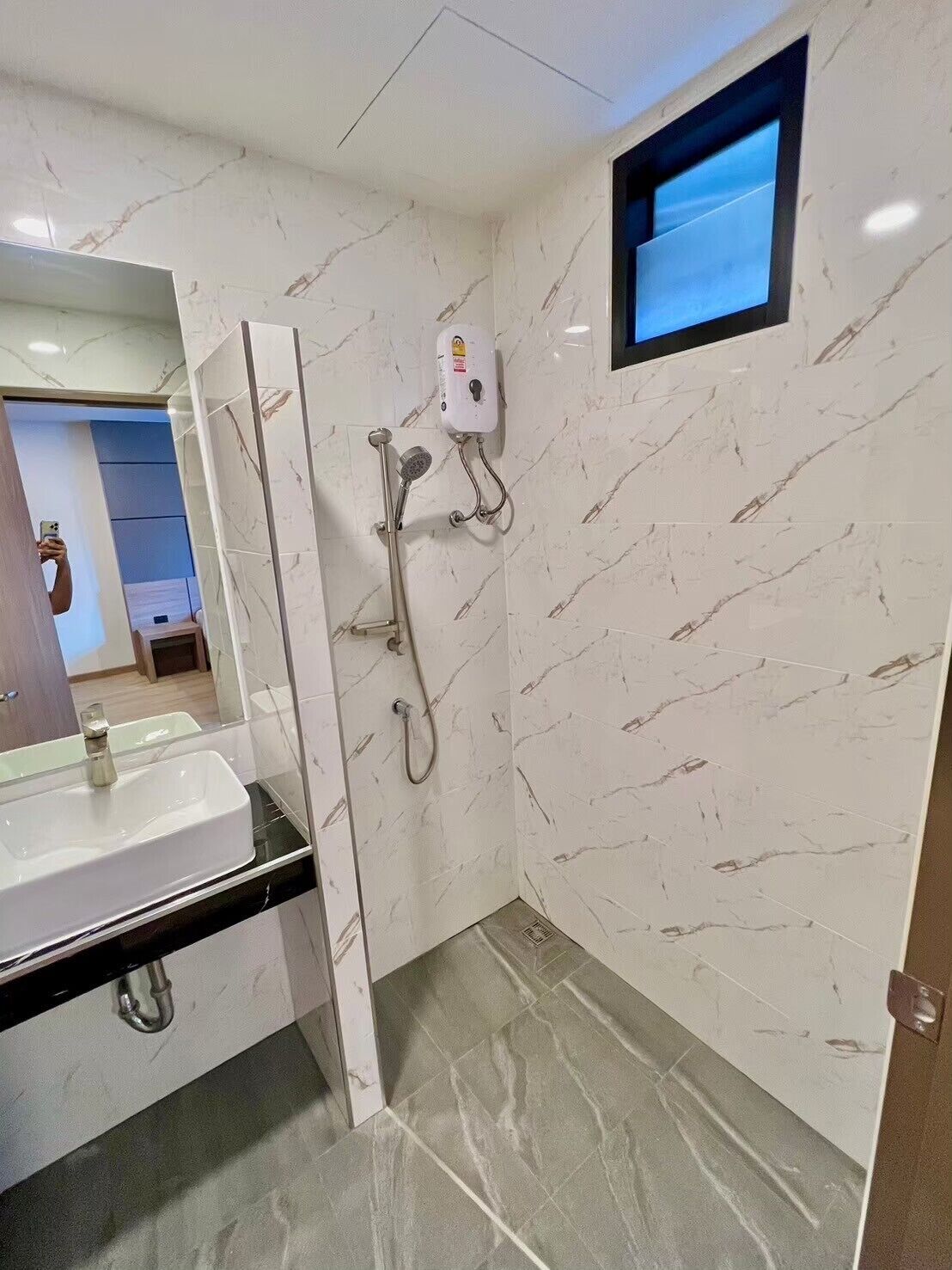 Un baño con pared de mármol blanco, lavamanos con encimera negra y ducha de mano.
