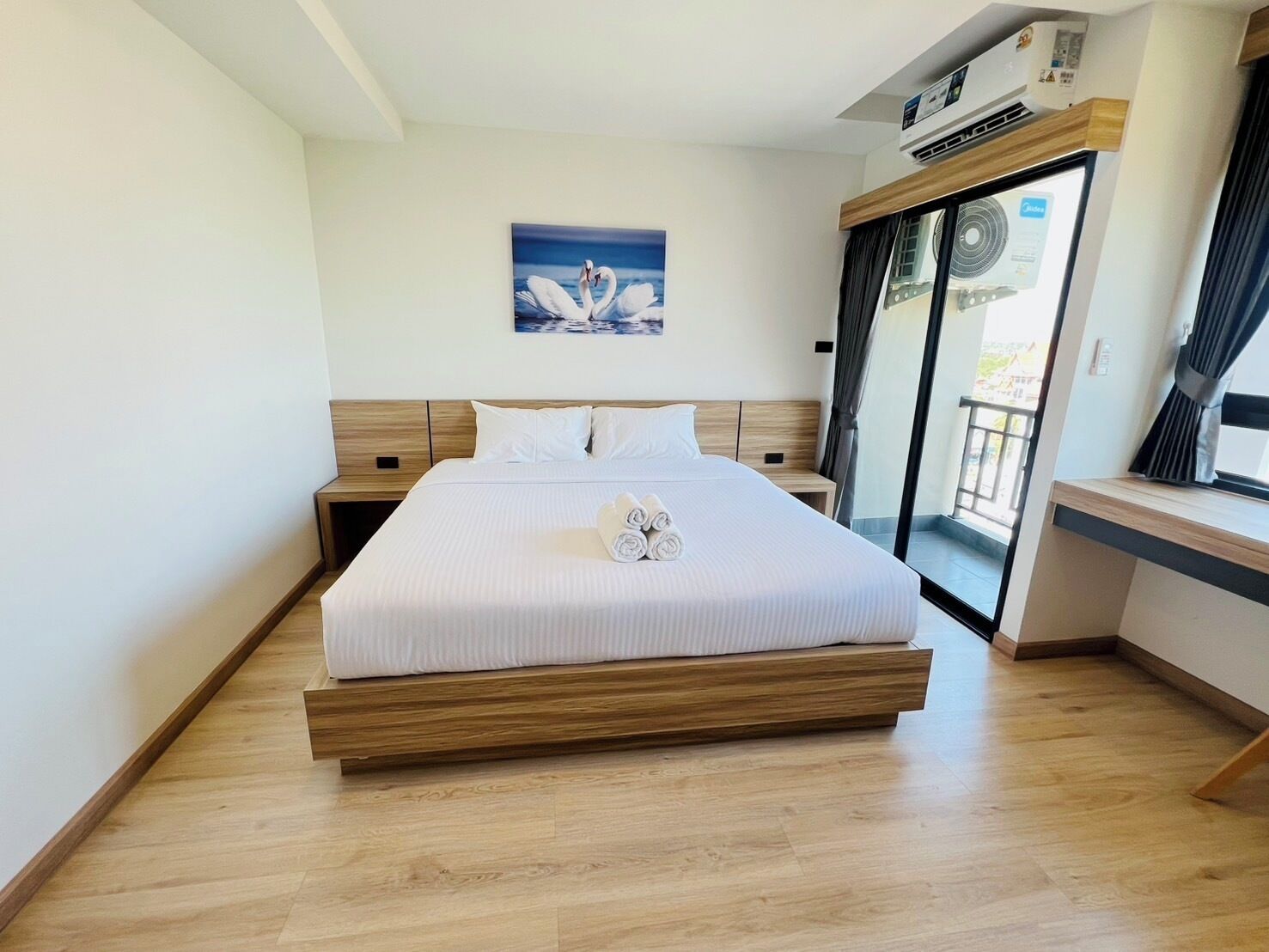 A modern hotel room with a large bed, a view through a glass door, and a painting on the wall.