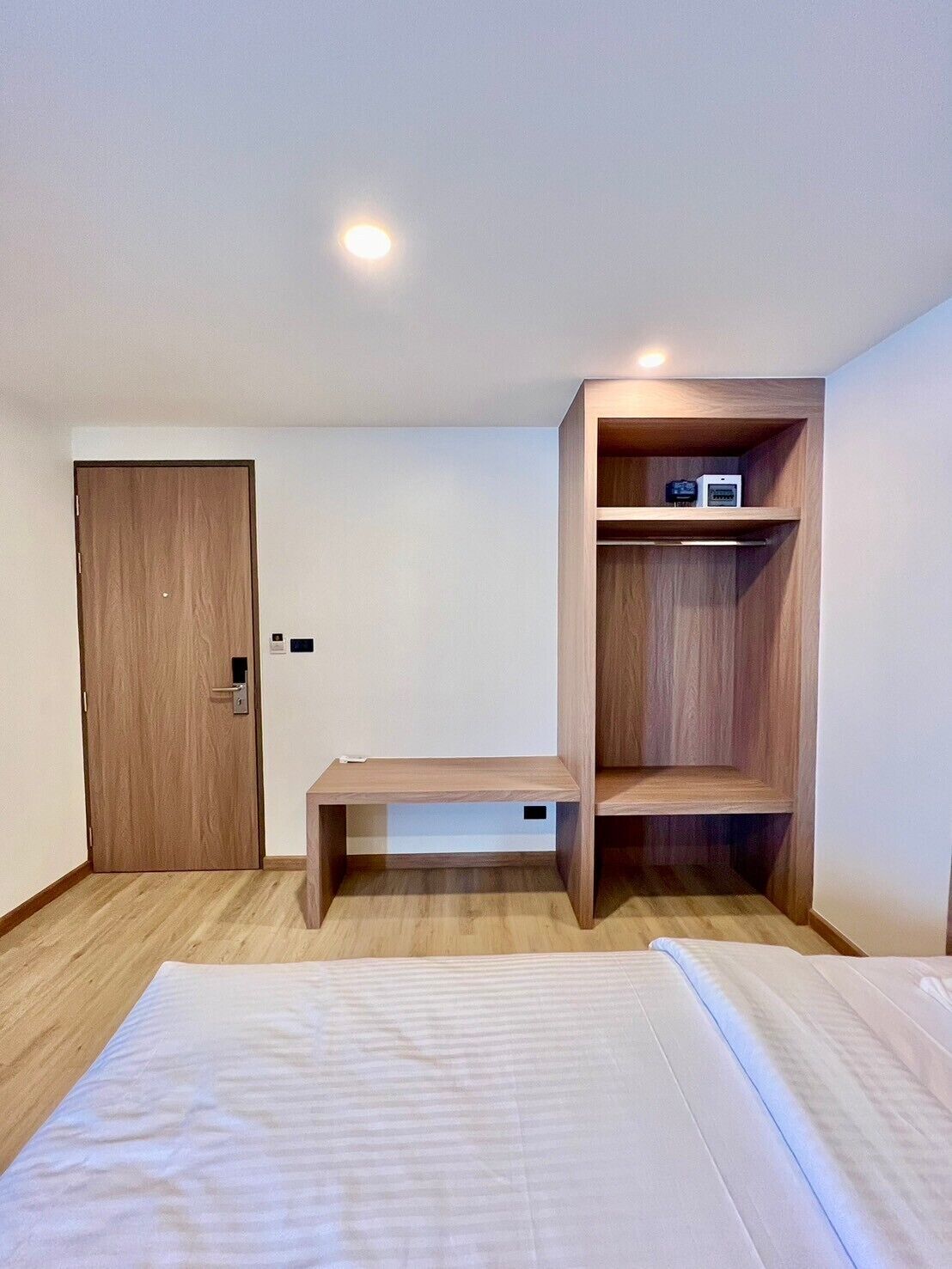 A bedroom with a bed, a wooden wardrobe, a bench, and a small shelf with a device.