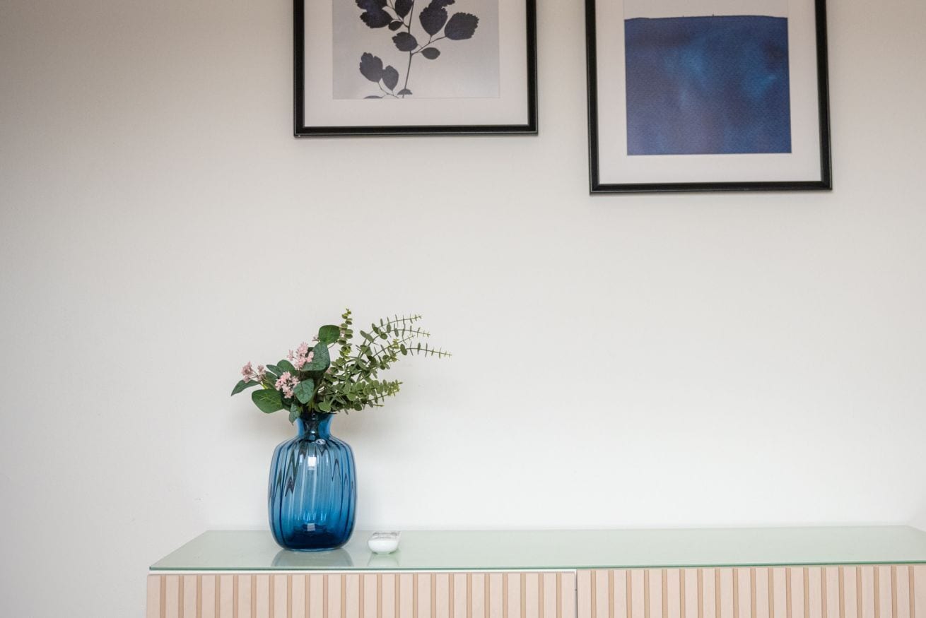 Un vaso blu con fiori su un tavolo di vetro, con un muro bianco e due quadri incorniciati.