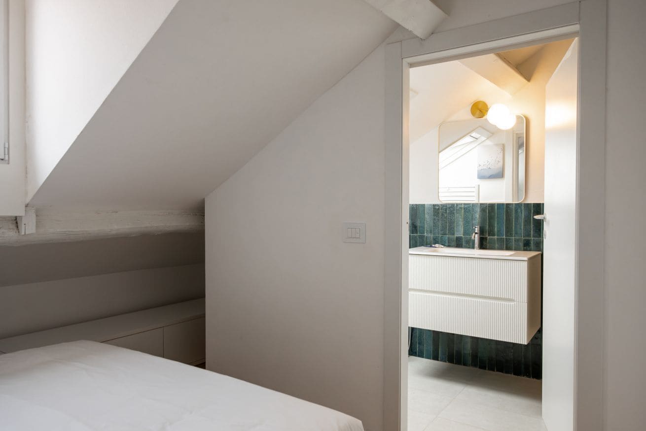 Una camera da letto con soffitto a falde, un letto e una piccola finestra.