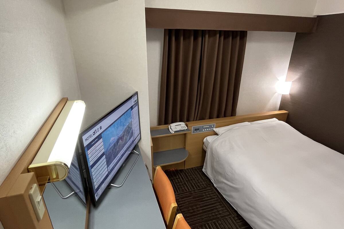 A hotel room with a bed, a desk with a computer, a telephone, and a wall-mounted TV.