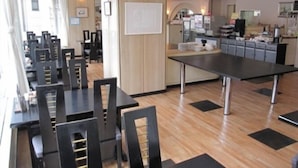 A modern restaurant with black tables and chairs, wooden flooring, and a kitchen area in the background. - Hotel Alpha-One Mishima (Mishima)