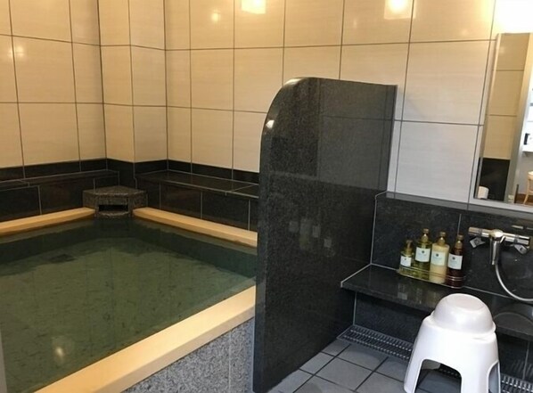 A spa area with a large soaking tub, a small step leading into the tub, and a shelf with toiletries. - Hotel Alpha-One Takaoka (Takaoka)