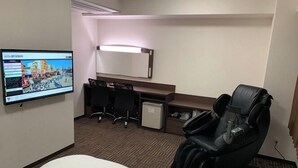 Habitación de hotel con cama, escritorio con dos sillas, sillón de masaje, televisor y un refrigerador pequeño.
