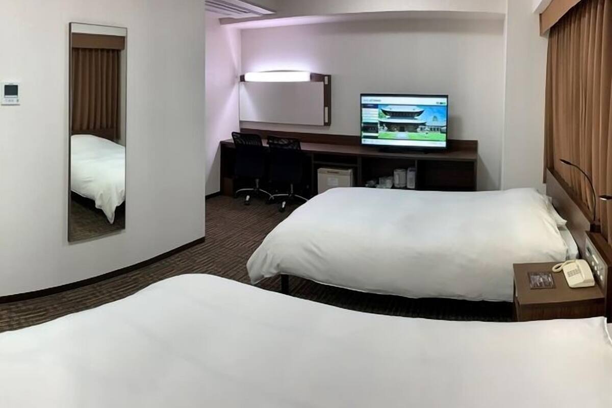 A hotel room with two beds, a desk, a television, and a mirror.