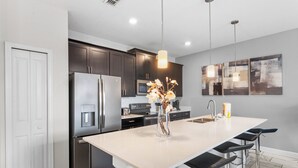A modern kitchen with dark cabinets, stainless steel appliances, a large island with bar stools, and pendant lighting. - Golf  & splash vacation homes, close to Disney (Kissimmee)