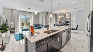 A modern kitchen with a large island, stainless steel appliances, and a view to the outdoor seating area. - Golf  & splash vacation homes, close to Disney (Kissimmee)