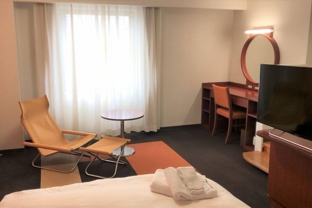 A hotel room with a bed, a desk, a chair, a TV, and a window with curtains.