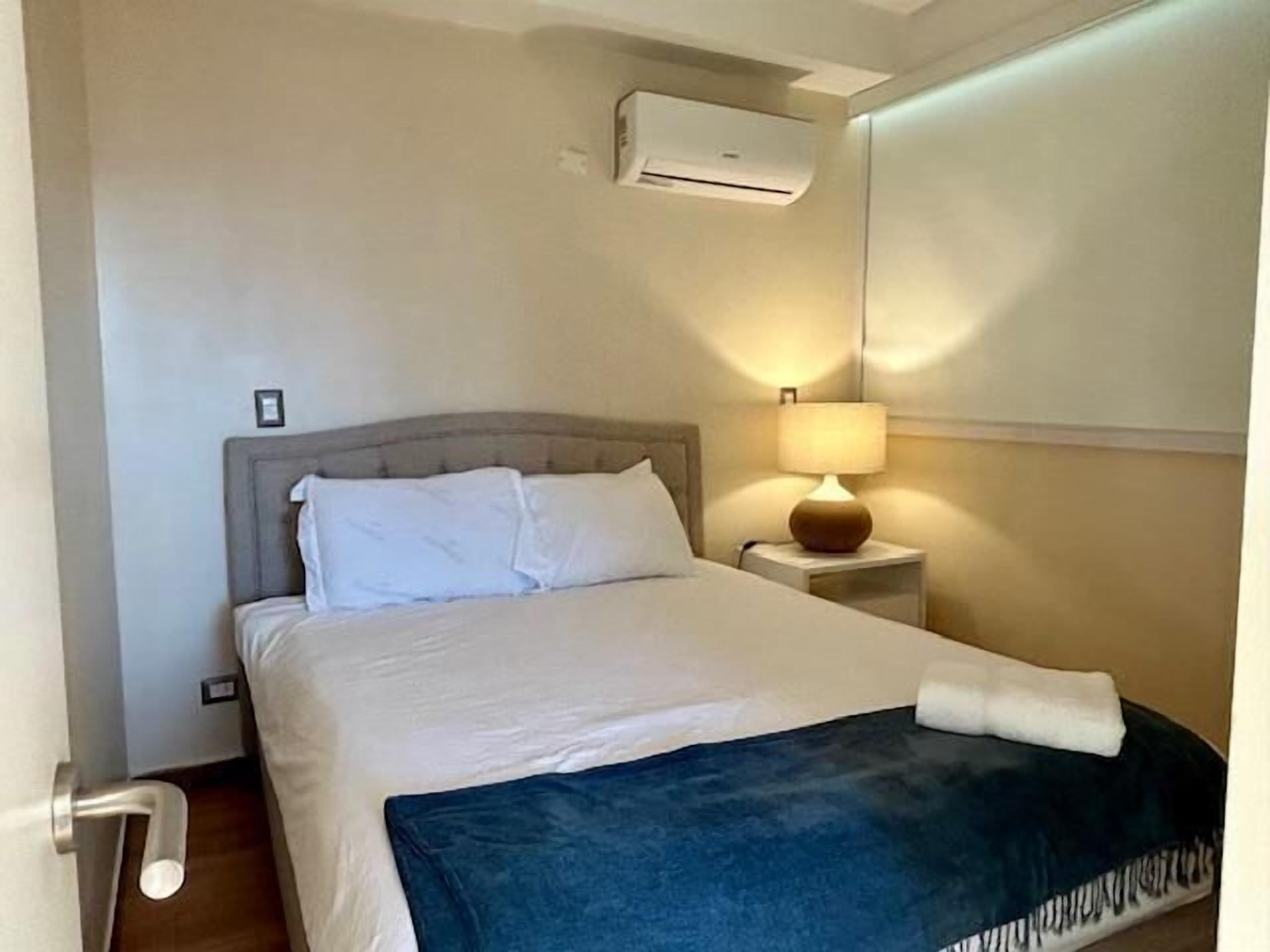 Une chambre d’hôtel avec un lit, une table de chevet avec une lampe et un appareil de climatisation fixé au mur.