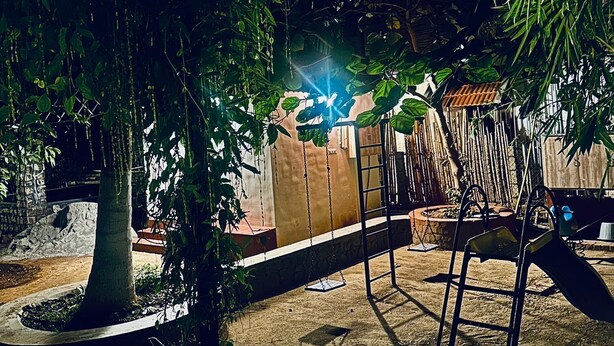 A playground with a swing set and a slide, surrounded by trees and a concrete border. - Bamboo Nest (Pollachi)