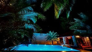 A nighttime view of a pool area with palm trees and a building with warm lighting. - Bamboo Nest (Pollachi)