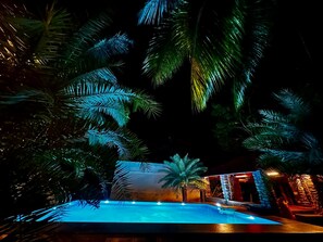 A nighttime view of a pool area with palm trees and a building with warm lighting. - Bamboo Nest (Pollachi)