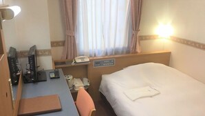 Habitación de hotel con cama, escritorio, teléfono, lámpara y una silla.