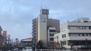 Un hotel con un llamativo letrero con la letra 'P' que indica estacionamiento, una torre del reloj y un edificio moderno con un letrero que dice 'Stationary Shop'.