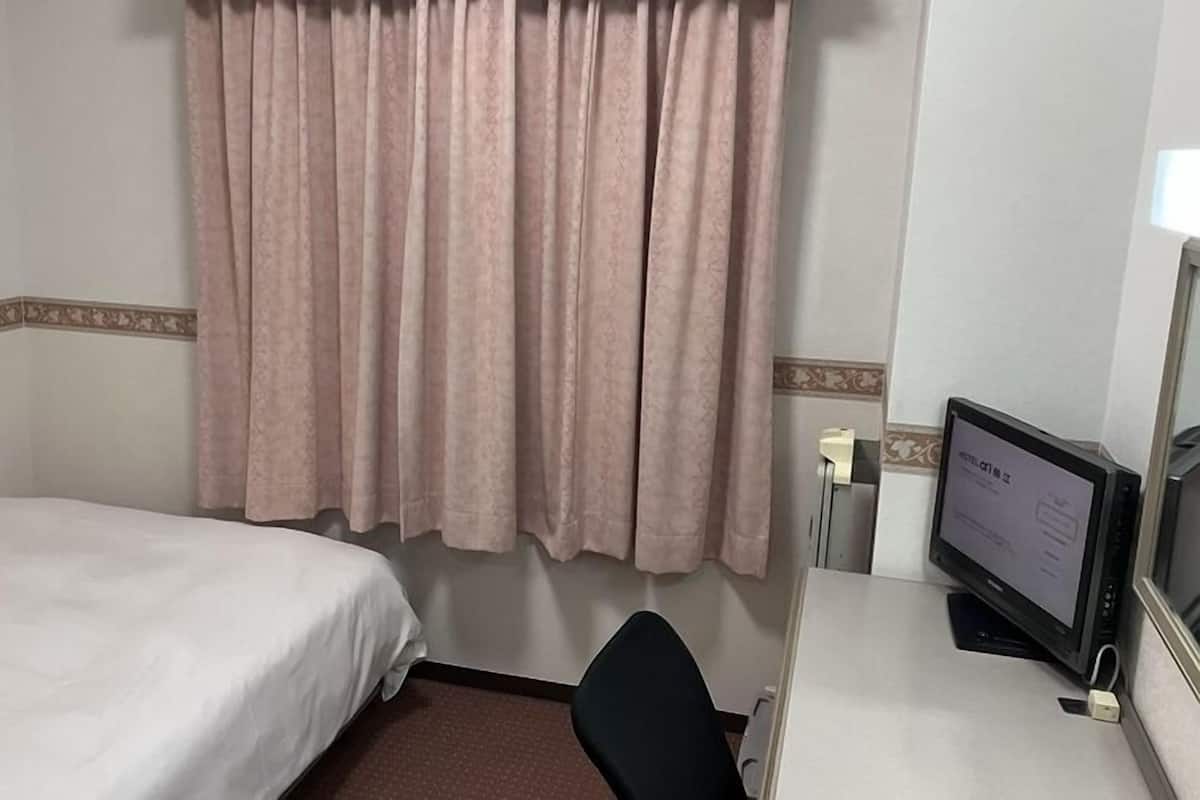 A hotel room with a single bed, a desk with a computer, and a window with curtains.