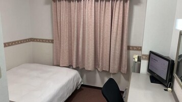 Quarto de hotel com uma cama de solteiro, uma mesa com computador e janela com cortinas.
