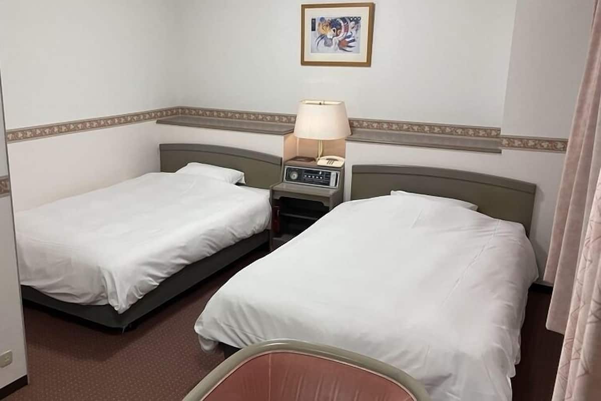 A hotel room with two single beds, a bedside table with a lamp, a small table with a phone, and a picture on the wall.