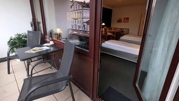 A room with a bed, a desk with a chair, a small table with a chair, and a potted plant.