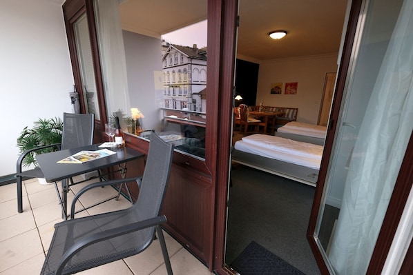 A room with a bed, a desk with a chair, a small table with a chair, and a potted plant.