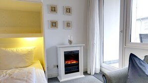 A hotel room with a bed, a small fireplace, a window with curtains, and wall-mounted pictures.