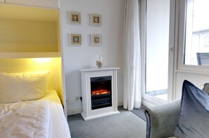 A hotel room with a bed, a small fireplace, a window with curtains, and wall-mounted pictures. - Am Strand Studio 30 - 1-room vacation apartment in the heart of Westerland. - only 250 (Westerland)