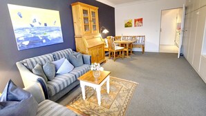 A living room with a sofa, a wooden cabinet, a dining table with chairs, and a rug.