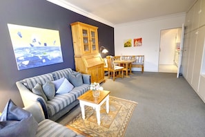 A living room with a sofa, a wooden cabinet, a dining table with chairs, and a rug.