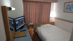 Habitación de hotel con cama, escritorio, computadora, teléfono y ventana con cortinas.