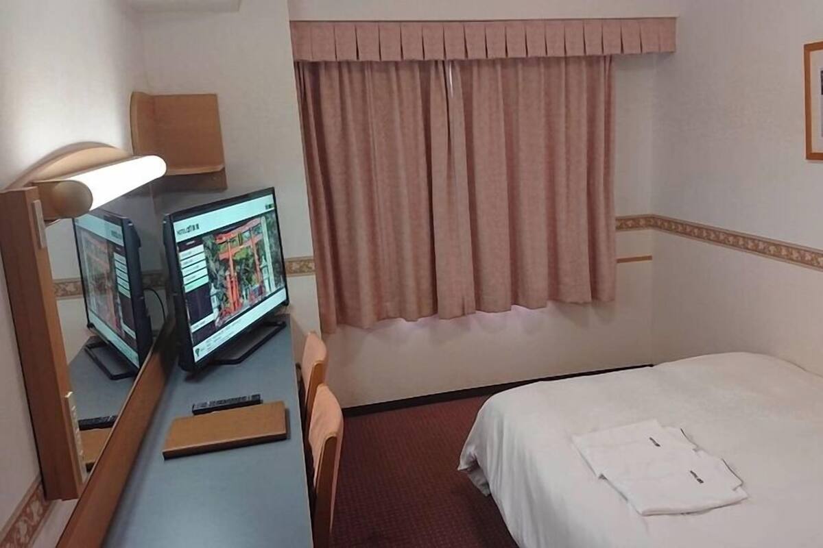 Une chambre d’hôtel avec un lit, un bureau avec un ordinateur, une fenêtre avec des rideaux et un tableau encadré au mur.