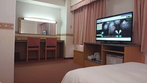 Habitación de hotel con cama, escritorio y silla, televisor mostrando fuegos artificiales, y un espejo.