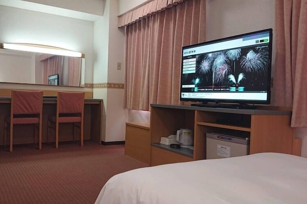 Une chambre d’hôtel avec un lit, un bureau et une chaise, un téléviseur diffusant un feu d’artifice et un miroir.