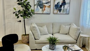 A living room with a beige sofa, a round coffee table, a potted plant, and abstract art on the wall. - Charming 3-bedroom cottage in fantastic Las Vegas with Pool (Las Vegas)