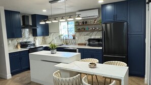 A modern kitchen with dark blue cabinets, a white island, and a dining area with two upholstered chairs. - Charming 3-bedroom cottage in fantastic Las Vegas with Pool (Las Vegas)