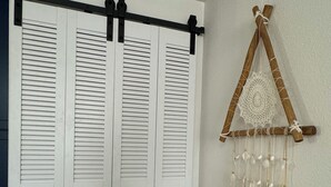 A room with a white closet featuring horizontal louvered doors and a wooden wall hanging with a geometric design and hanging elements. - Charming 3-bedroom cottage in fantastic Las Vegas with Pool (Las Vegas)