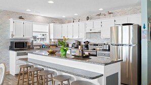 Una cocina moderna con armarios blancos, un refrigerador de acero inoxidable grande, una encimera de granito y una isla central con taburetes.