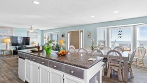 Una cocina amplia con una isla grande, comedor con sillas y un televisor.