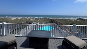 Terraza con piscina, con vistas a una playa con sombrillas y un cielo despejado.