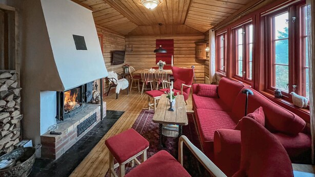 A cozy cabin interior with a fireplace, wooden walls, a dining area, and a seating area with red upholstered furniture. - Awesome home in Lillehammer with sauna (Lillehammer)