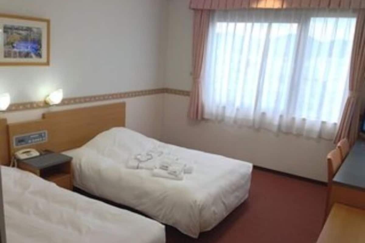 Una habitación de hotel con dos camas, una mesita de noche con teléfono y una ventana con cortinas.